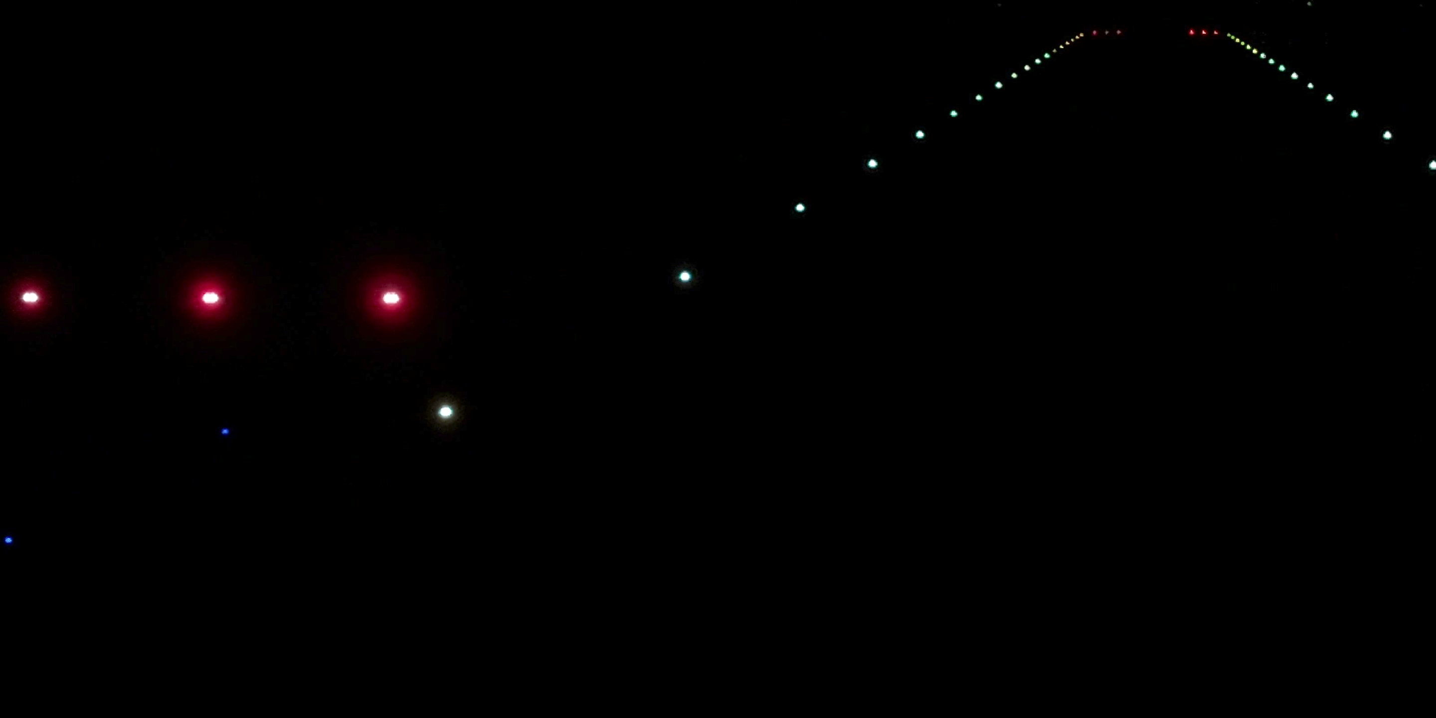 Real drone frame at night: PAPI units in the foreground and rows of runway lights converging towards the far end