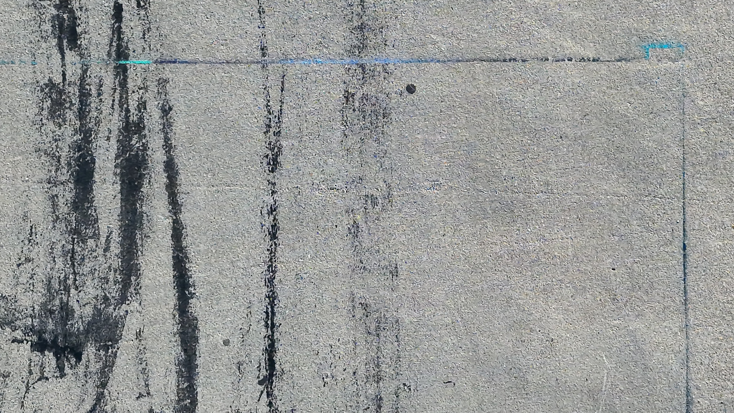 Prawdziwe zdjęcie z nadiru: beton z ciemnymi śladami opon biegnącymi w dół kadru i dylatacją płyt