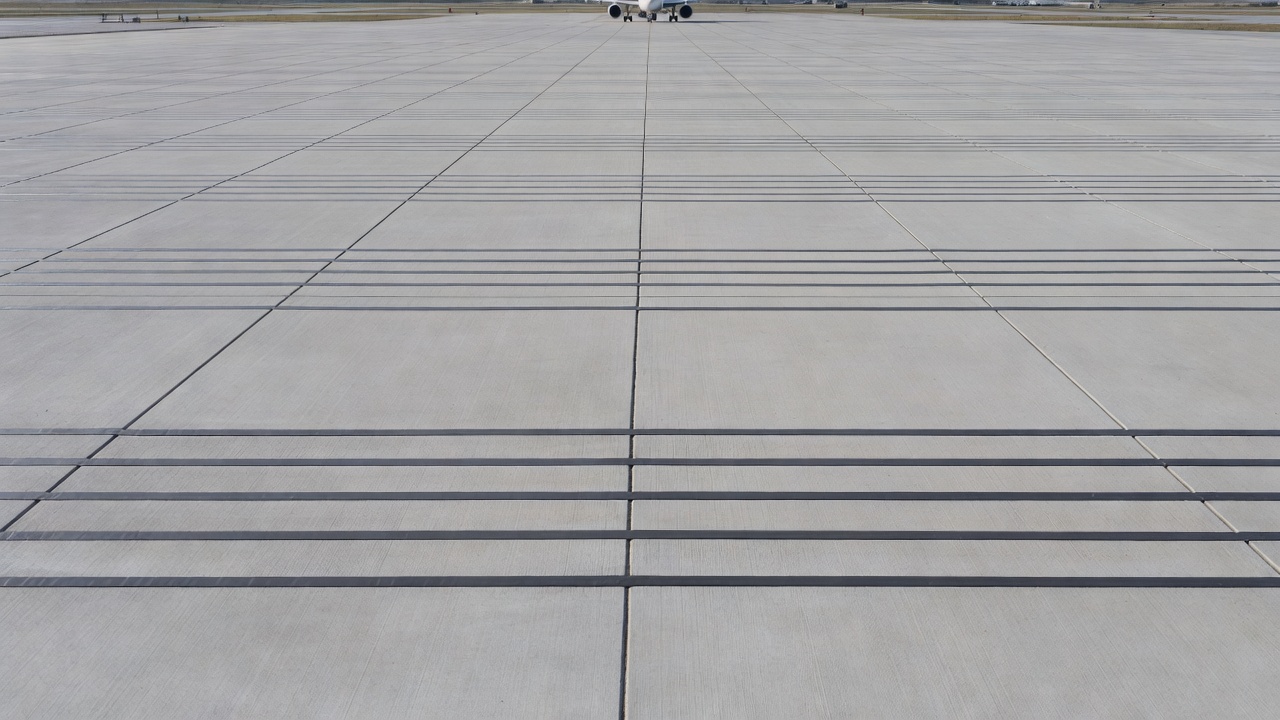 Aire de trafic aéroportuaire montrant une chaussée en béton avec des joints transversaux et longitudinaux scellés au silicone, avion à réaction en arrière-plan