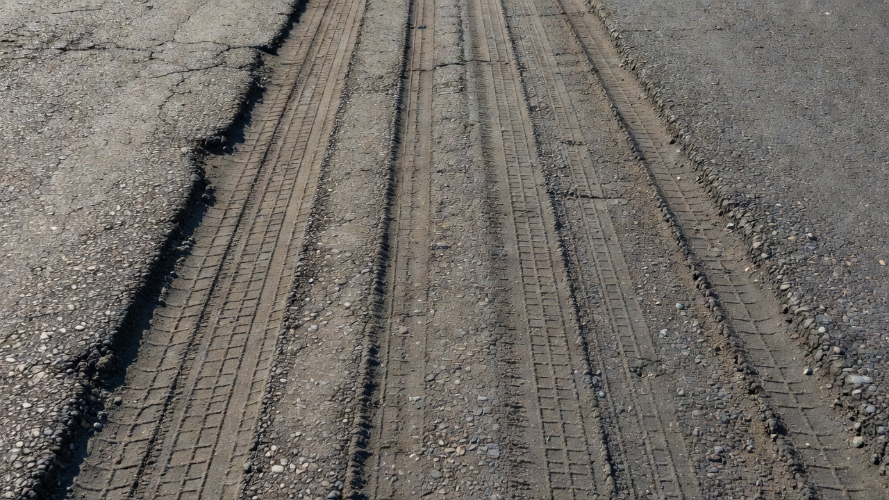 Gros plan de la surface d'une chaussée bitumineuse montrant des dépressions d'orniérage longitudinales dans les passages de roues avec des traces de pneus visibles