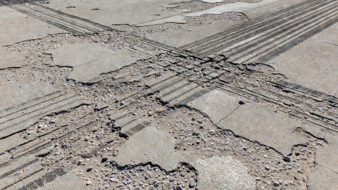Gros plan d'une surface de chaussée aéroportuaire en béton abrasée montrant des granulats exposés et l'usure de surface due à la friction des pneus