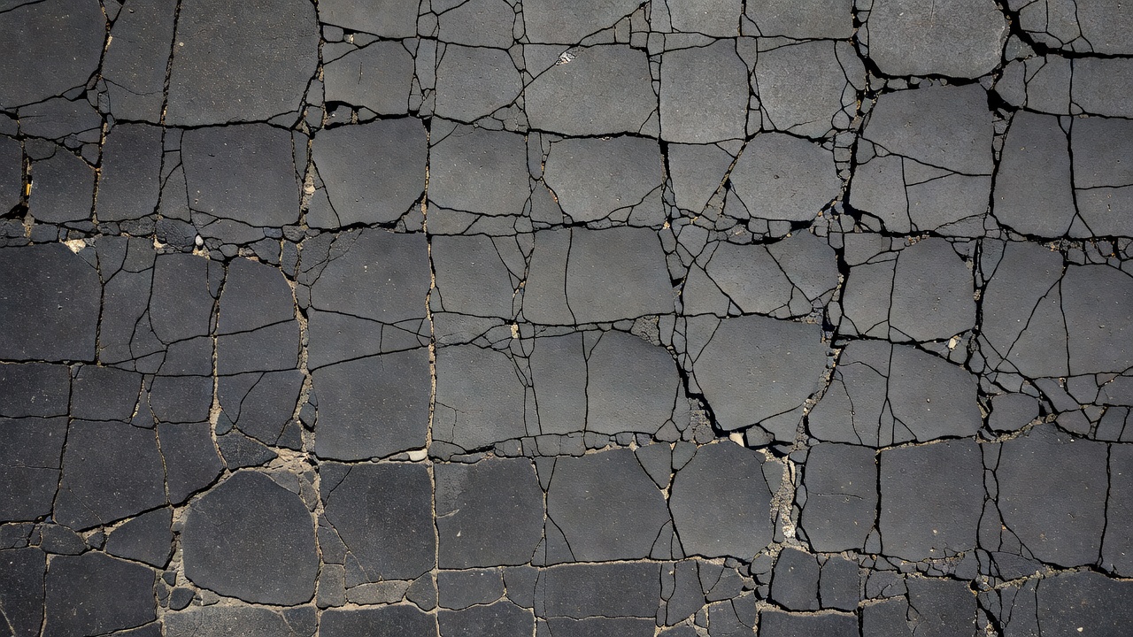 Fissuration en blocs sévère dans une chaussée en asphalte avec fissures larges et bords écaillés en motif rectangulaire