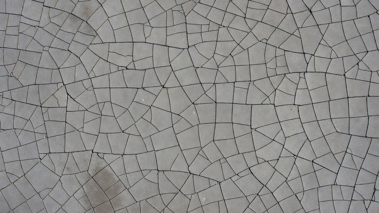 Fissures de retrait de dessiccation formant un motif de fissuration en cartes sur une surface de dalle en béton avec de fines fissures polygonales interconnectées