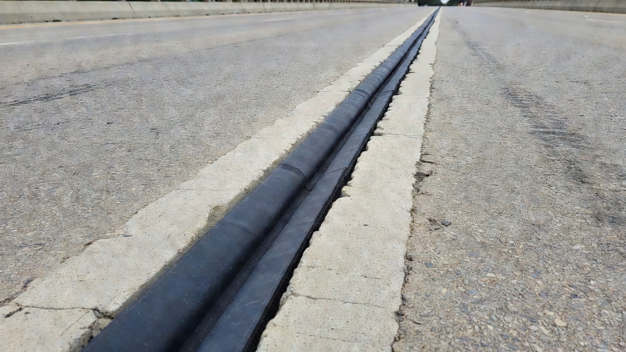 Détail d'un joint de dilatation de pont montrant un joint de compression en néoprène noir installé dans l'espace entre deux sections de tablier de pont en béton formant un joint étanche