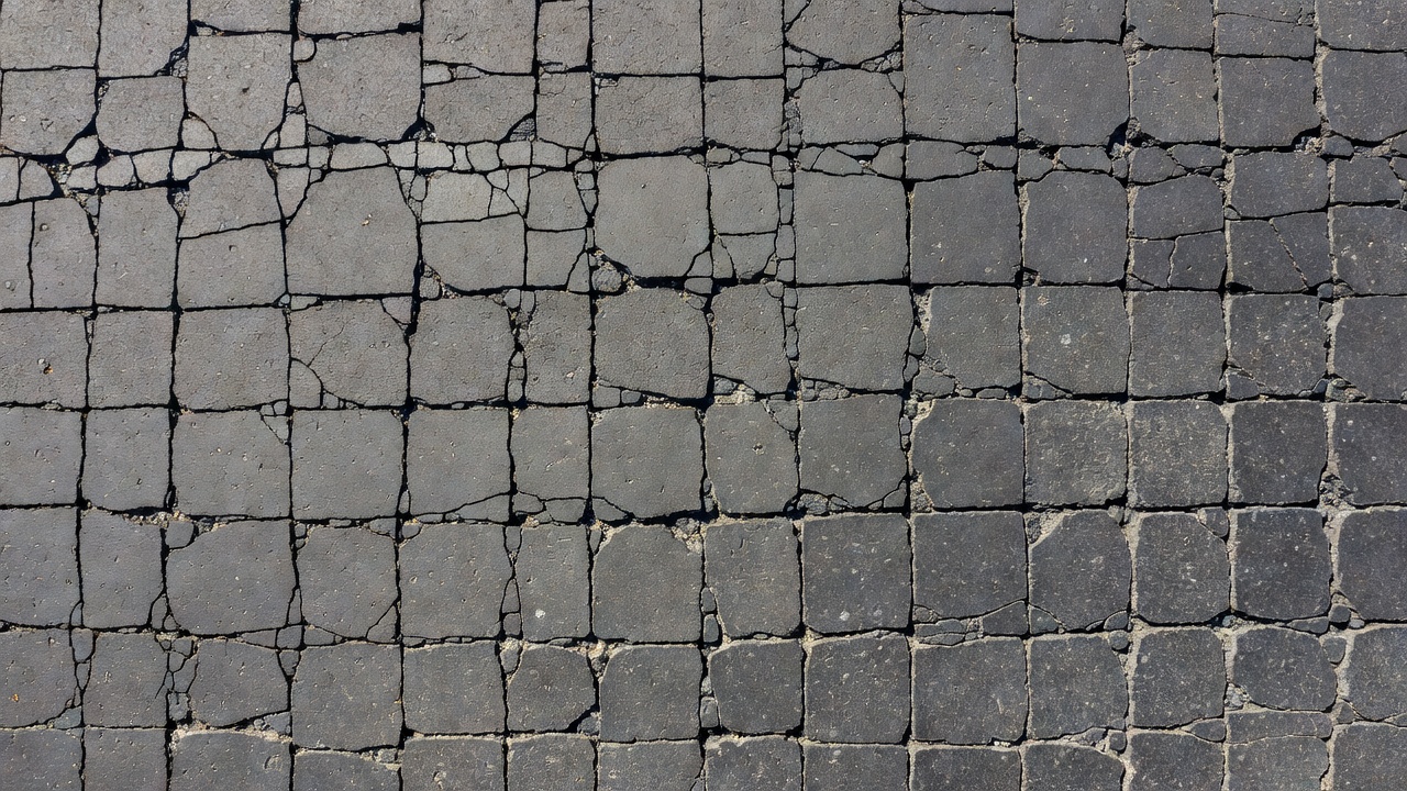 Vue aérienne d'une chaussée en asphalte avec motif de fissuration en blocs montrant des fissures rectangulaires interconnectées divisant la surface en blocs