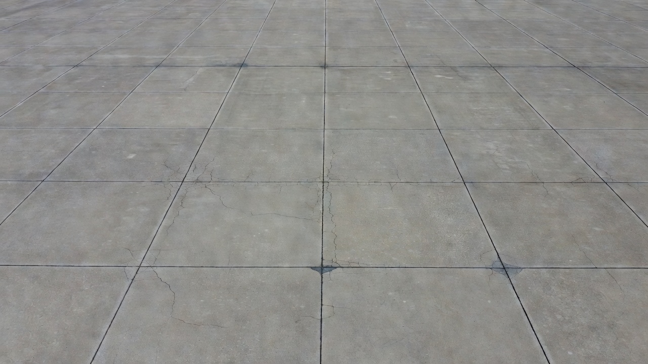 Vue aérienne d'une piste aéroportuaire en béton avec des joints de contraction et de fines fissures de retrait visibles près des lignes de joint