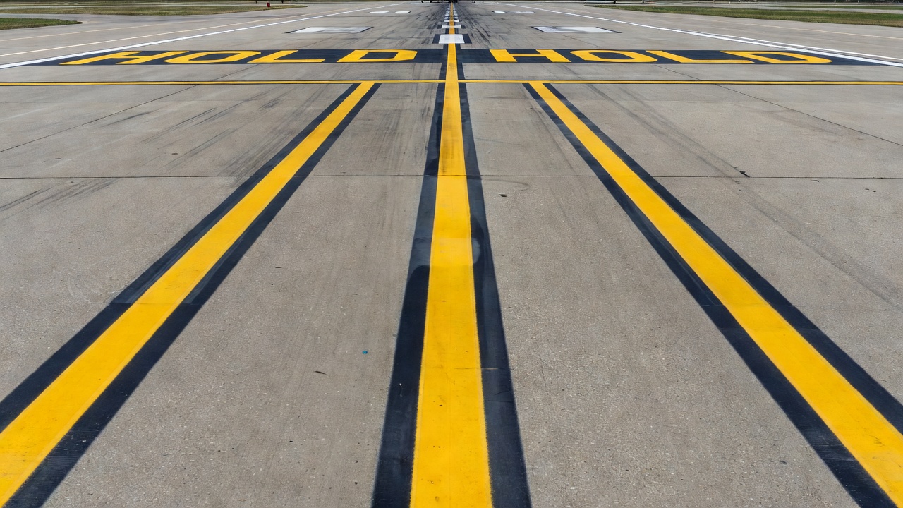 Close-up view of airport taxiway with yellow centerline marking and enhanced taxiway centerline with dashed yellow lines on both sides approaching a runway holding position