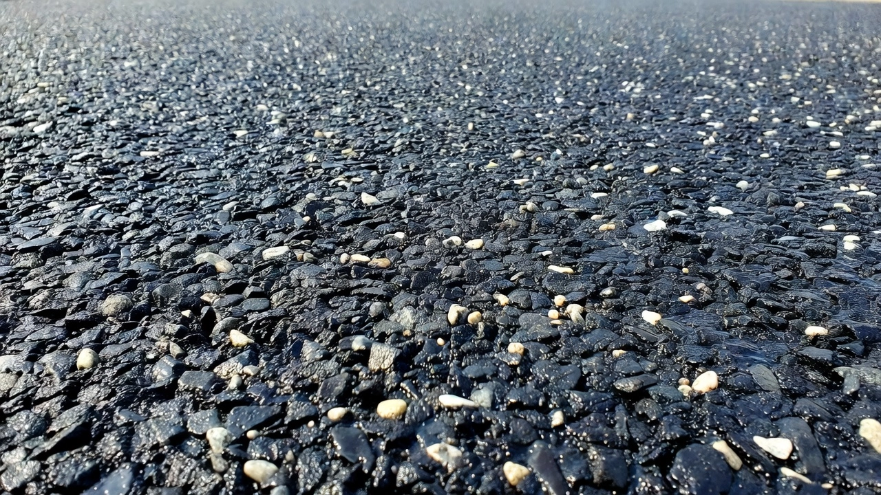 Photographie macro en gros plan d'une surface de chaussée par scellement gravillonné montrant des gravillons de pierre concassée incrustés dans un liant bitumineux noir créant une macrotexture rugueuse antidérapante