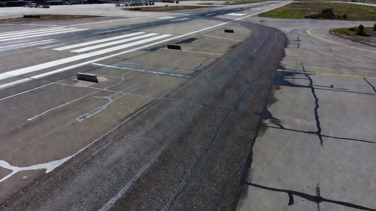 Vue aérienne par drone d'une route périphérique de piste d'aéroport avec traitement de surface par scellement gravillonné, petit aéroport régional, marquages de bord de piste, entretien de chaussée, texture de surface de tarmac visible