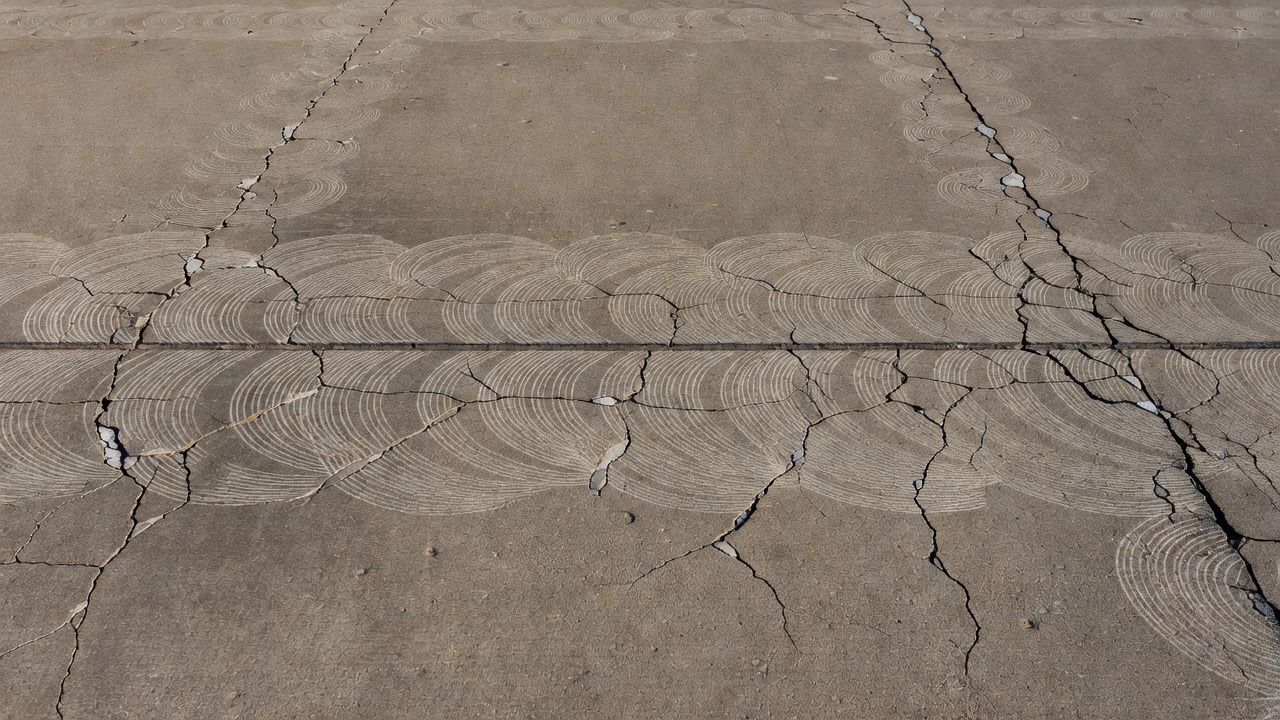 Detailní záběr vzoru D-crackingu na betonovém povrchu letištní dráhy ukazující půlměsícovité trhliny podél příčné spáry