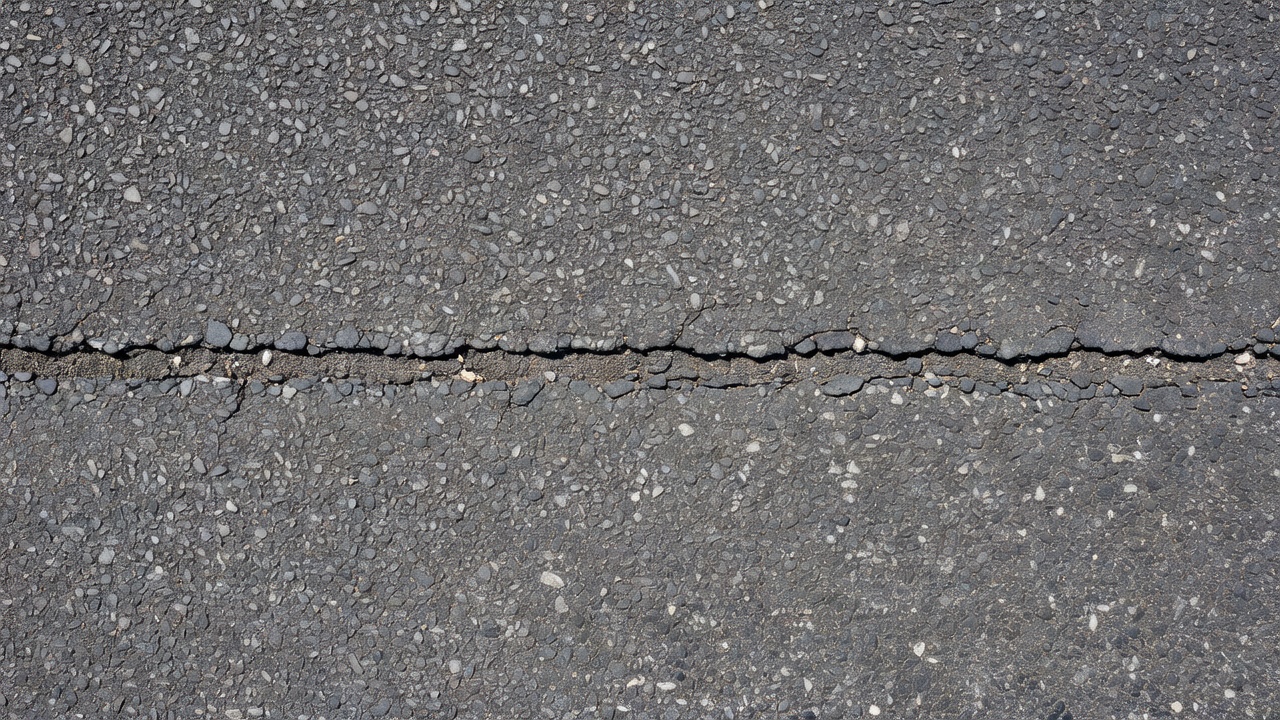 Close-up view of a transverse thermal crack on an asphalt pavement surface, running perpendicular to the road centerline