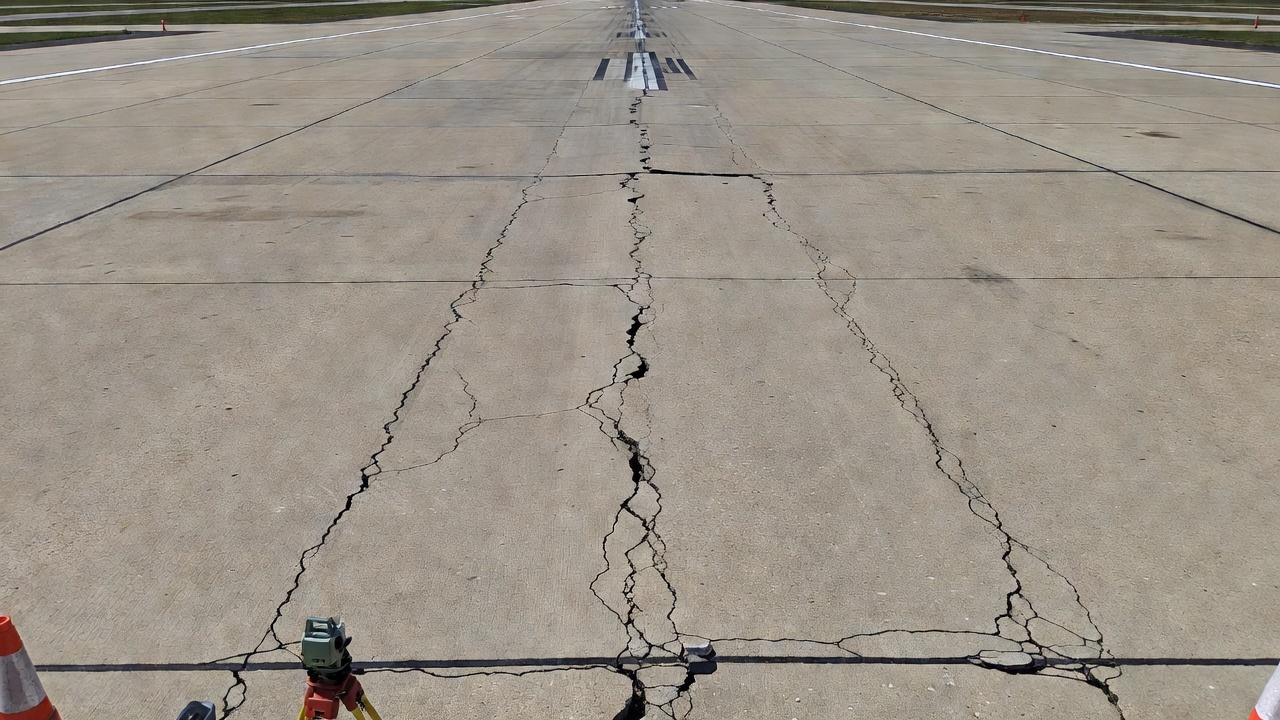 Chaussée de piste d'aéroport en béton présentant un tassement différentiel avec fissuration longitudinale et ressauts aux joints de chaussée